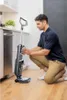 A man is kneeling in a kitchen, adjusting a vacuum cleaner. Voir les images du produit