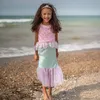 Mädchen im pink-türkisen Meerjungfrauenkostüm steht am Strand vor dem Meer und lächelt in die Kamera. Produktbild-Vorschau