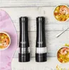 Two electric salt and pepper grinders are displayed on a wooden surface, with bowls of food and a napkin nearby. Náhled obrázku produktu