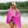 A woman is standing on a beach, wrapped in a pink towel, with a lake and trees in the background. Produktbild-Vorschau