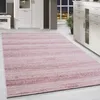 A pink and white striped rug is laid out on a light wooden floor in a modern living room. White furniture and a large window with a city view at night are visible in the background.