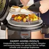 A person is using a multi-cooker to prepare food, with food items on racks inside the appliance. Produktbild-Vorschau