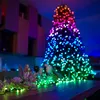 A Christmas tree decorated with colorful lights and a garland of decorative flowers on a wooden surface. Náhled obrázku produktu