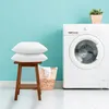 Two pillows are stacked on a wooden stool next to a washing machine and a laundry basket. Produktbild-Vorschau