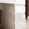 A close-up view of a white dresser with multiple drawers, showing the glossy finish and clean lines. The side of the dresser is a matte gray. Produktbild-Vorschau