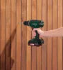 A hand holding a cordless drill against a wooden wall. Produktbild-Vorschau
