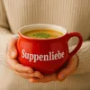 Hands holding a red soup mug filled with soup. Voir les images du produit
