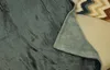 A close-up view of a folded gray blanket with a sherpa lining, resting on a couch with a patterned pillow in the background. Podgląd zdjęcia produktu