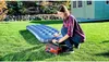 A woman is inflating an air mattress in a backyard with a house in the background. Voir les images du produit
