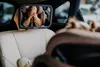 A child is visible in a car seat mirror, covering their eyes. Produktbild-Vorschau