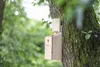 A wooden birdhouse is attached to a tree trunk in a forest setting. Produktbild-Vorschau