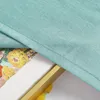 A close-up view of a green fabric draped over a framed artwork with yellow and orange flowers, and two lemons in the foreground. Produktbild-Vorschau