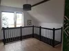 A wooden railing in a loft or attic space with a window and a hanging lamp. Produktbild-Vorschau