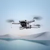 A white drone flies over a body of water with snow-capped mountains in the background. Náhled obrázku produktu