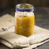 A jar of preserves sits on a burlap cloth with a spoon to the side. Voir les images du produit