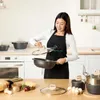 A woman in a kitchen is holding a pot and lid from a cookware set. Produktbild-Vorschau
