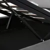 A close-up view of the hydraulic lift mechanism of a bed frame, showing the gas strut and metal supports. Produktbild-Vorschau