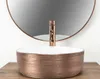 A close-up shot of a rose gold vessel sink with a copper faucet, set against a blurred background with a mirror. Produktbild-Vorschau