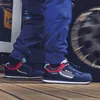A person wearing blue pants and Sparco Martini racing shoes stands on a wooden deck next to a spinning tire. Produktbild-Vorschau