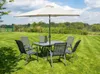 A garden table and chairs set with a large umbrella, set up on a manicured lawn under a partly cloudy sky. Produktbild-Vorschau