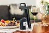 A Coravin wine preservation system is placed on a table next to a cheese board and wine glasses. Podgląd zdjęcia produktu