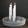 Four white candles are lit and placed in a round, light gray candle holder on a wooden surface. Produktbild-Vorschau