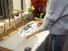 A person is rinsing a cleaning device in a kitchen sink under a faucet. Produktbild-Vorschau