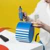 A person is using a hot glue gun to attach a blue and white striped band to a cylindrical object. Voir les images du produit