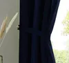 A close-up of a dark blue curtain held back by a tie-back, with a hint of greenery visible through the window. Produktbild-Vorschau