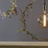 A decorative LED wreath with flowers and lights hangs above a wooden surface. Produktbild-Vorschau