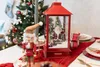 A festive Christmas table setting with a nutcracker, a red lantern with a Santa Claus figurine inside, and a decorated Christmas tree in the background. Produktbild-Vorschau