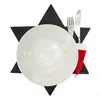 A place setting with a plate, cutlery, and a Christmas-themed Santa hat cutlery holder, arranged on a star-shaped placemat. Produktbild-Vorschau