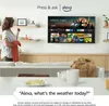 A woman is holding a remote and a cloth, standing in front of a large TV screen displaying a streaming service interface. The TV is mounted on a wall above a wooden cabinet. In the foreground, there is a sofa and a table with mugs and a plate. Náhľad obrázku produktu