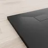 A close-up, angled view of a black shower tray with a textured surface, placed on a light wooden floor. Produktbild-Vorschau