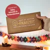 A hand holding an advent calendar box, with a string of small advent calendar envelopes hanging in the foreground. Produktbild-Vorschau