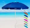 A blue beach umbrella is displayed on a sandy beach with the ocean and sky in the background. Several smaller umbrellas in various colors are arranged to the right of the main umbrella. Voir les images du produit