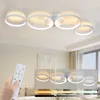 A hand holding a remote control in front of a modern ceiling light fixture with multiple rings, with smaller inset images showing different lighting effects. Voir les images du produit