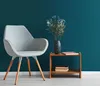 A modern gray armchair sits next to a small wooden side table with a vase of flowers and books on it, against a teal textured wall. Produktbild-Vorschau