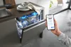 A person is using a smartphone to control a dishwasher in a modern kitchen. Anteprima dell’immagine prodotto