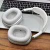 A pair of silver and white headphones are placed on top of a silver laptop keyboard, with a wooden surface visible below. Podgląd zdjęcia produktu