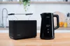 A black electric kettle and a black toaster are displayed on a wooden countertop in a kitchen setting. Anteprima dell’immagine prodotto