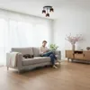 A man is sitting on a couch in a living room, looking at his phone. A cat is sleeping on the couch next to him. A modern pendant light hangs from the ceiling. Náhľad obrázku produktu