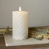A white LED candle with a swirling pattern sits on a marble slab, surrounded by dried grasses and wheat. Produktbild-Vorschau
