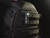 A black tactical backpack with a small black flashlight attached to the MOLLE webbing. Produktbild-Vorschau
