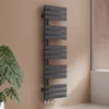 A modern anthracite designer radiator is shown mounted on a light brown wall next to a large green plant. A bathtub and shower screen are visible in the background. Podgląd zdjęcia produktu