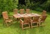 A wooden dining set with chairs and a table is set up on a lawn in a garden. Produktbild-Vorschau