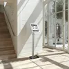 A tablet stand is placed in a well-lit indoor space with a staircase and large windows. Anteprima dell’immagine prodotto
