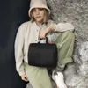 A woman sitting on rocks, holding a black toiletry bag. Produktbild-Vorschau