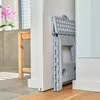 A gray folding stool is leaning against a white wall in a hallway. A wooden stool and a potted orchid are visible in the background. Náhľad obrázku produktu