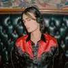 A person wearing headphones sits on a tufted leather couch. Voir les images du produit
